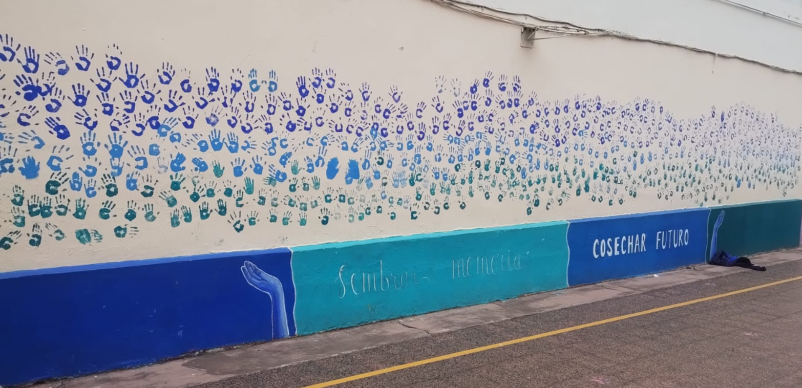 Mural del colegio con manos pintadas y el mensaje Sembrar memoria, cosechar futuro