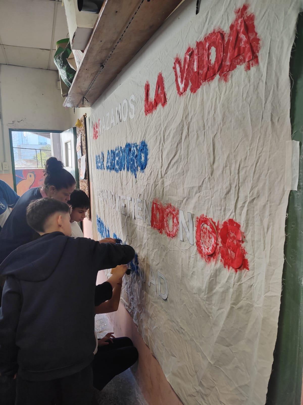 Una docente y dos alumnos terminando de pintar las letras del lema